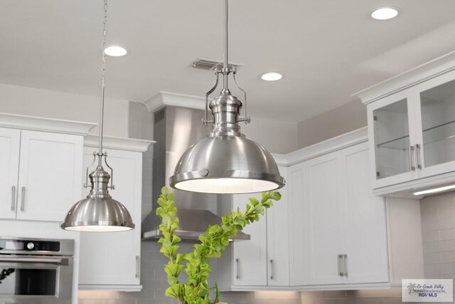 interior details featuring recessed lighting, white cabinetry, stainless steel oven, hanging light fixtures, and glass insert cabinets