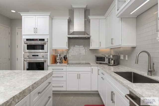 kitchen with stainless steel appliances, wall chimney range hood, a sink, and white cabinets