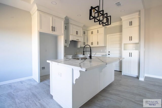 kitchen with visible vents, light stone counters, a kitchen island with sink, white cabinetry, and a sink