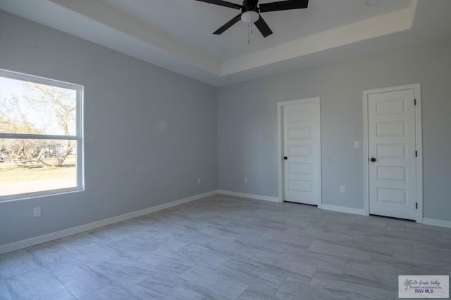 unfurnished bedroom featuring a tray ceiling, a ceiling fan, and baseboards