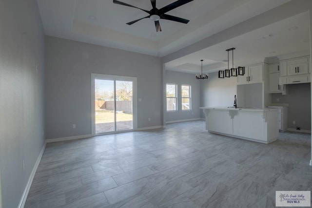 unfurnished living room with ceiling fan with notable chandelier, a sink, a raised ceiling, and baseboards