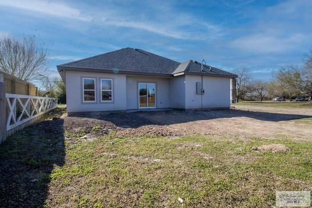 back of property with a shingled roof, a yard, and fence