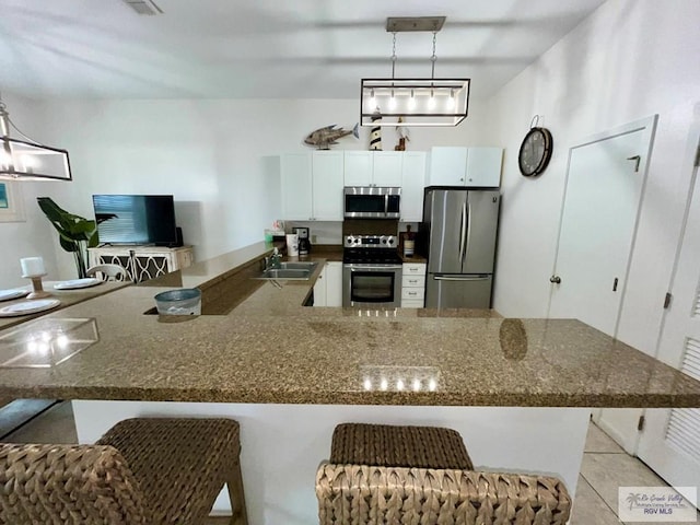 kitchen featuring a sink, a peninsula, dark stone counters, stainless steel appliances, and white cabinetry