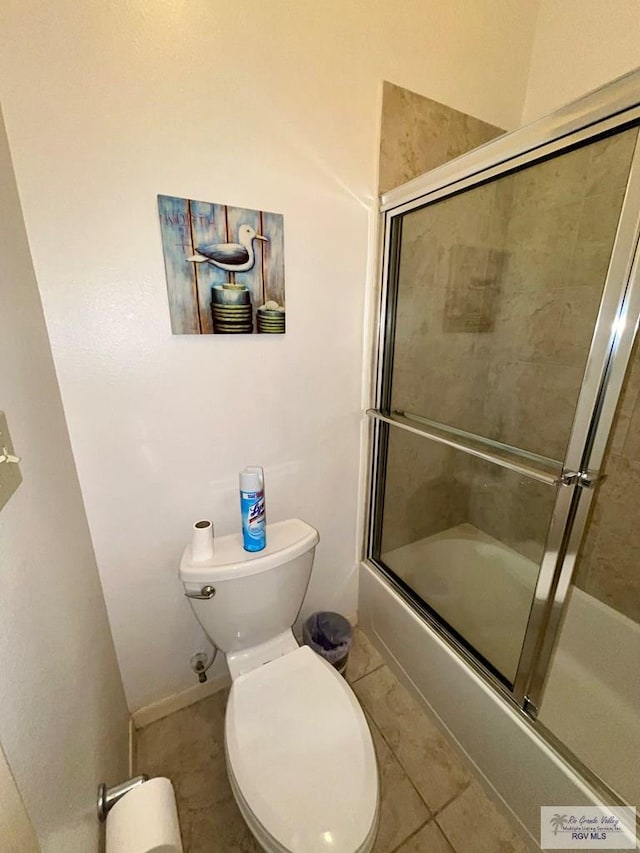 bathroom with tile patterned flooring, baseboards, toilet, and shower / bath combination with glass door