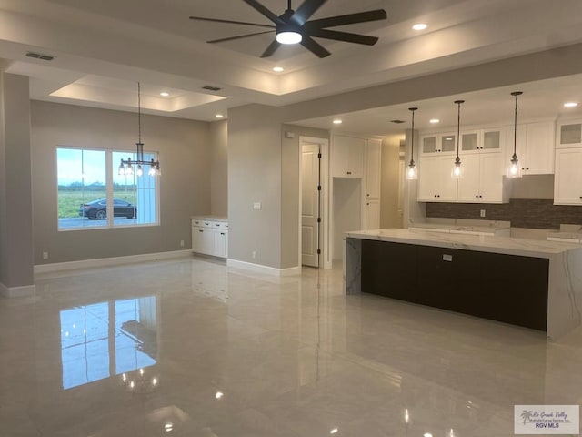 kitchen featuring ceiling fan with notable chandelier, white cabinets, a raised ceiling, and hanging light fixtures