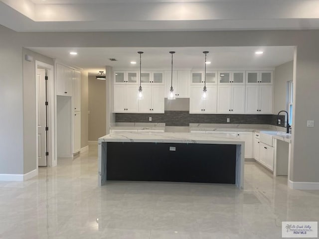 kitchen with hanging light fixtures, a center island, light stone counters, white cabinets, and sink