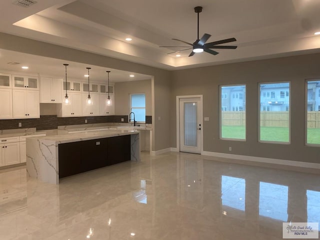 kitchen with a spacious island, light stone countertops, ceiling fan, a tray ceiling, and white cabinetry