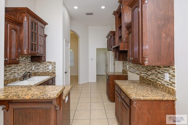 1508 W 20th St, Mission, TX 78572 - kitchen featuring arched walkways, light tile patterned flooring, decorative backsplash, glass insert cabinets, and baseboards