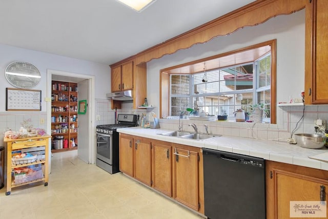 kitchen with tasteful backsplash, stainless steel gas range, sink, dishwasher, and tile counters