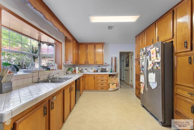 kitchen featuring stainless steel refrigerator, dishwasher, sink, and tile countertops