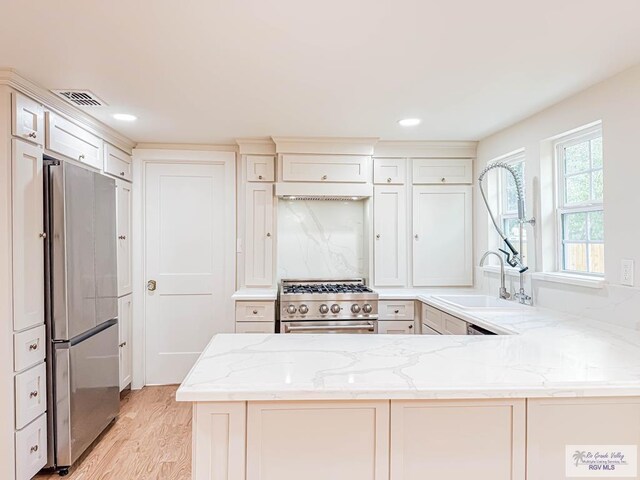 1214 W Lincoln Ave Unit 22, Harlingen, TX 78550 - kitchen featuring appliances with stainless steel finishes, a sink, light stone counters, light wood-type flooring, and a peninsula
