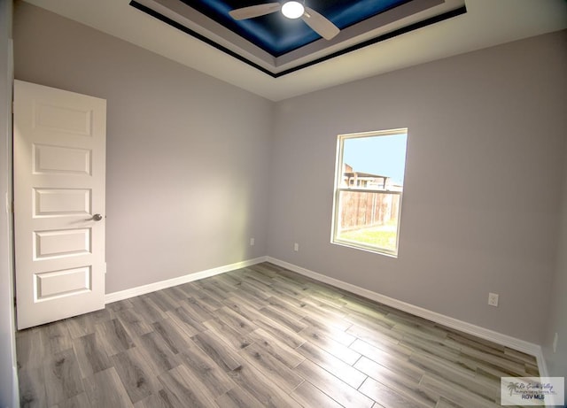 unfurnished room featuring wood finished floors, a raised ceiling, a ceiling fan, and baseboards