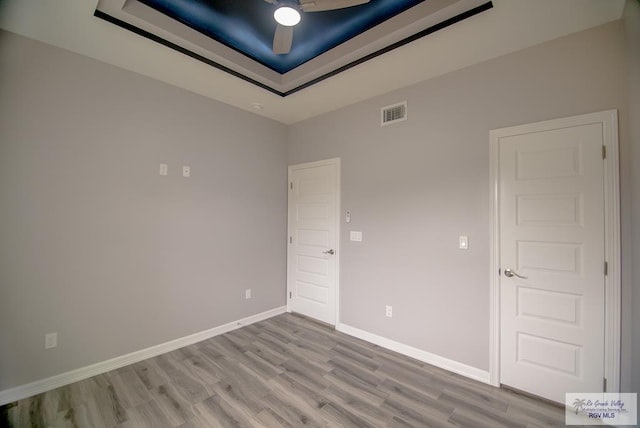 empty room with visible vents, baseboards, a raised ceiling, and wood finished floors