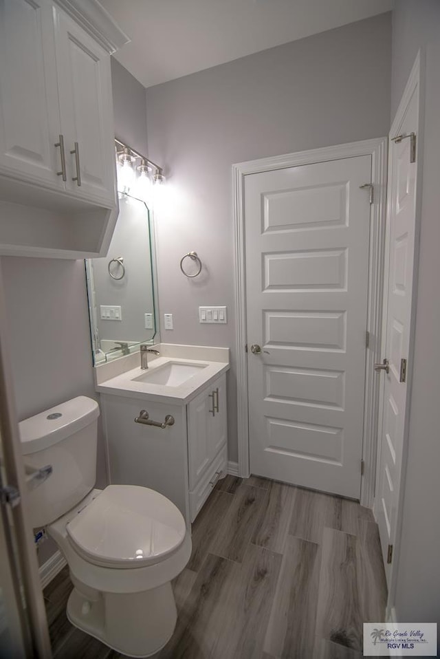 bathroom with toilet, wood finished floors, and vanity