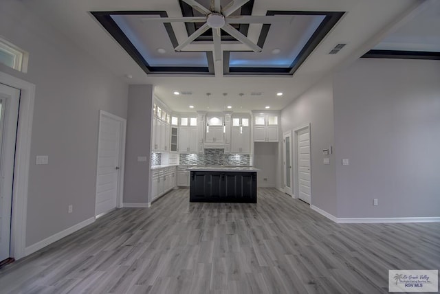 kitchen with a kitchen island, visible vents, white cabinetry, light countertops, and backsplash