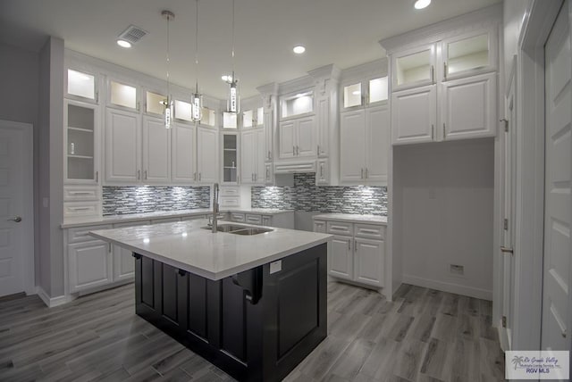 kitchen with visible vents, white cabinets, a sink, a kitchen island with sink, and backsplash