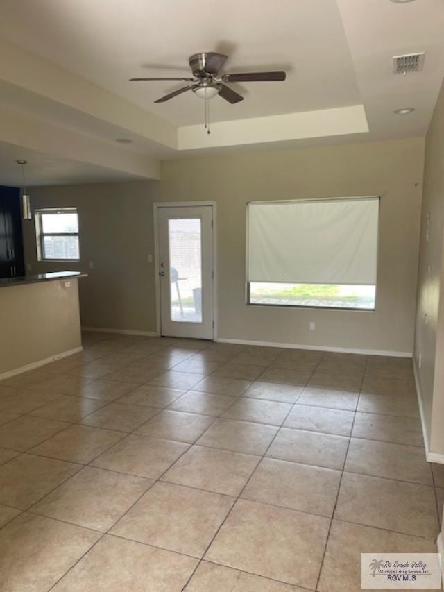 unfurnished room with a raised ceiling, ceiling fan, and light tile patterned flooring