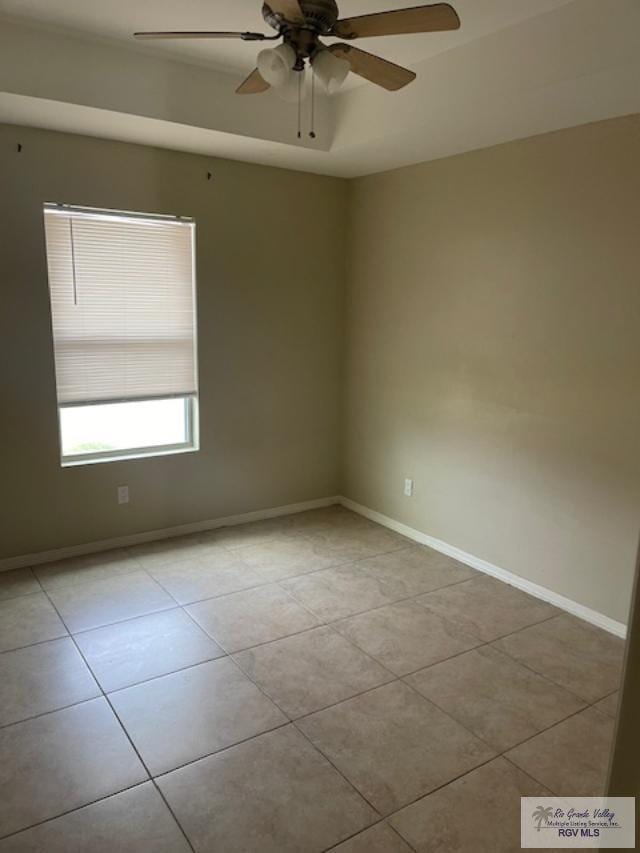 empty room featuring ceiling fan, a tray ceiling, and light tile patterned floors