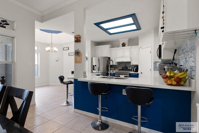 kitchen with a kitchen breakfast bar, backsplash, stainless steel appliances, a notable chandelier, and white cabinetry