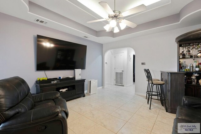 living room featuring a tray ceiling, bar, and ceiling fan