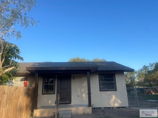 view of front of property featuring a shingled roof, fence, and stucco siding