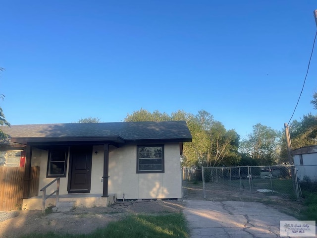 bungalow with a gate, roof with shingles, fence, and stucco siding