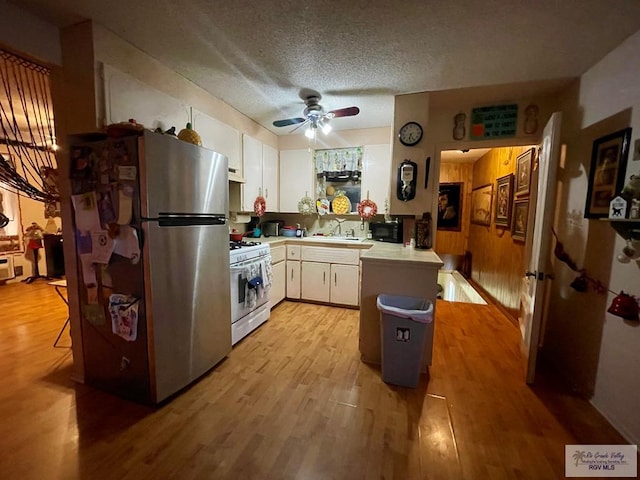 kitchen featuring white gas range, white cabinetry, ceiling fan, kitchen peninsula, and stainless steel fridge