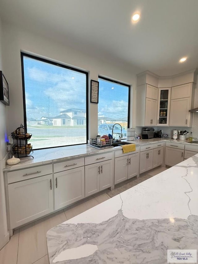 1992 Lulu St, Brownsville, TX 78577 - kitchen with a sink, light stone countertops, glass insert cabinets, white cabinets, and cooktop