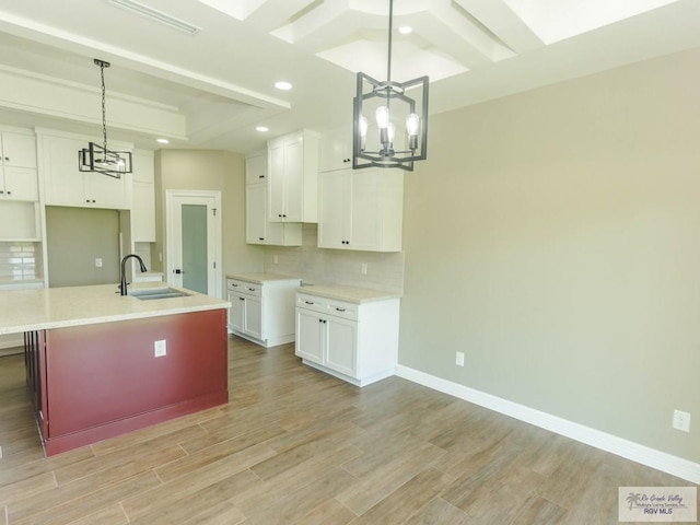 kitchen with sink, decorative light fixtures, white cabinetry, and an island with sink