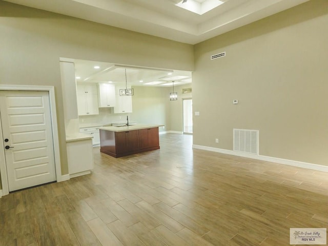 kitchen with decorative light fixtures, sink, white cabinetry, and a kitchen island with sink