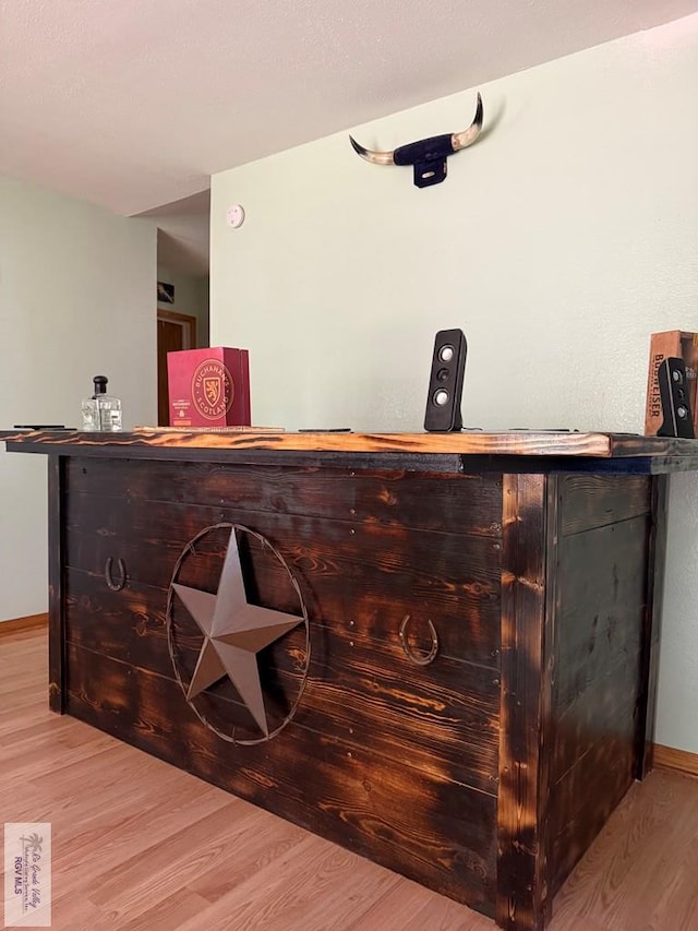 bar featuring light wood finished floors, a bar, and baseboards