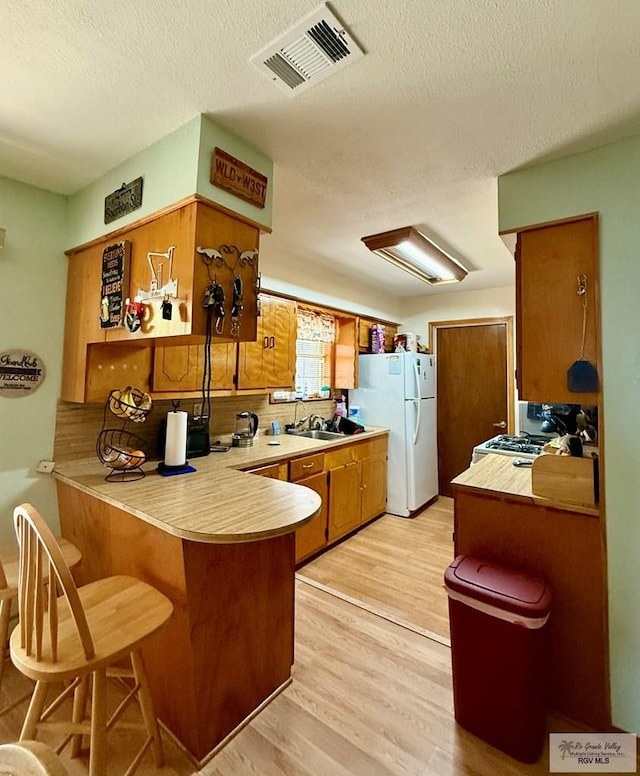 kitchen with visible vents, white appliances, a peninsula, light wood finished floors, and light countertops