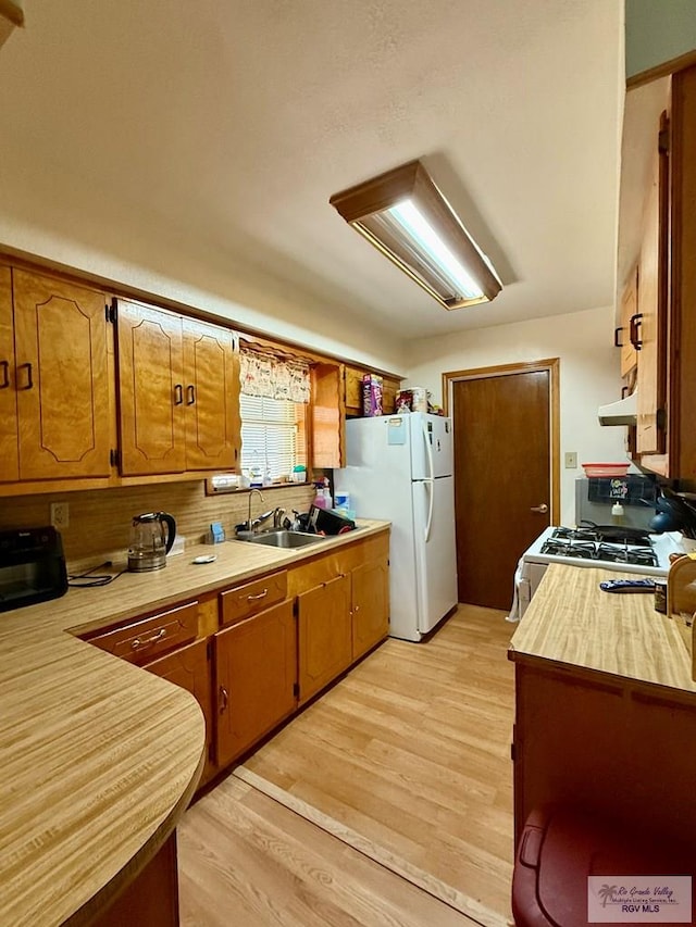 kitchen with white appliances, brown cabinetry, light countertops, and under cabinet range hood