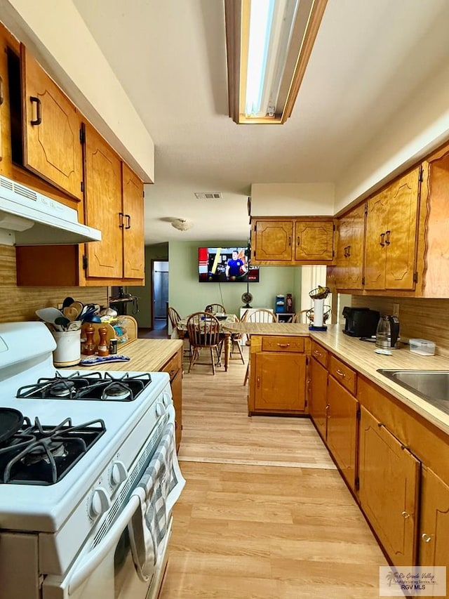 kitchen featuring visible vents, under cabinet range hood, brown cabinetry, light wood finished floors, and white gas range