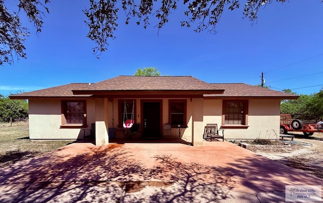 back of house with covered porch, stucco siding, and roof with shingles