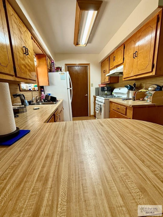 kitchen with white appliances, brown cabinetry, a sink, light countertops, and under cabinet range hood