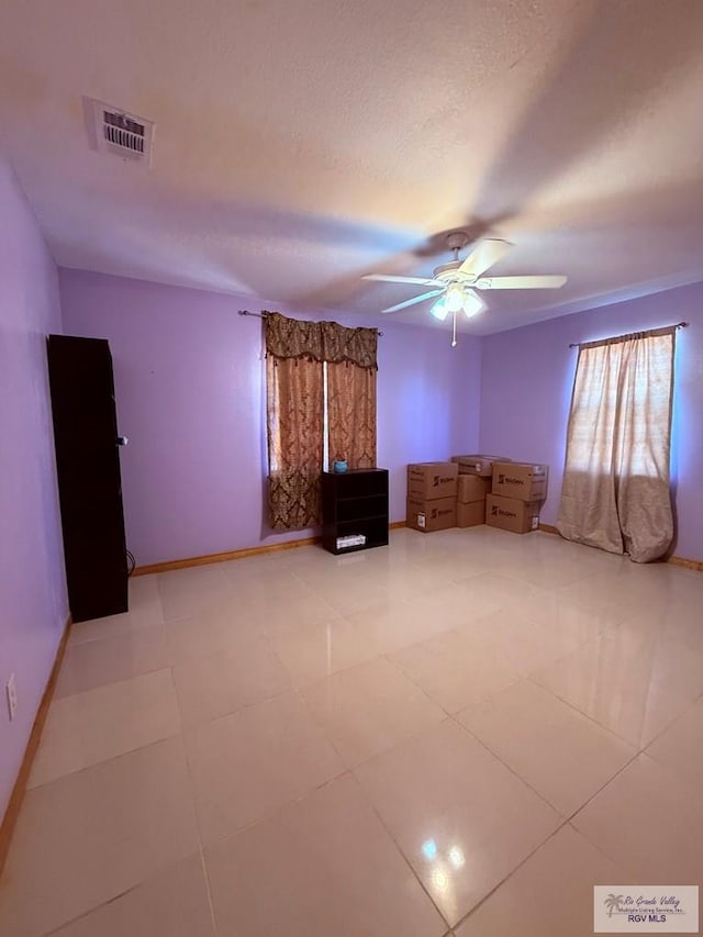 interior space with baseboards, a ceiling fan, visible vents, and a textured ceiling