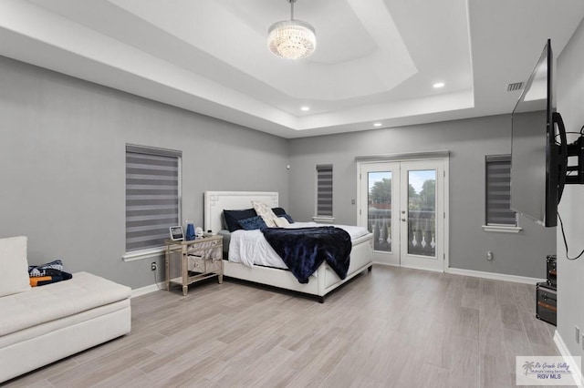 bedroom featuring a raised ceiling, a notable chandelier, access to exterior, and light wood-type flooring