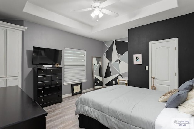 bedroom with ceiling fan, a tray ceiling, and light hardwood / wood-style flooring