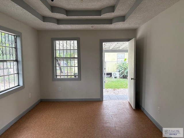 unfurnished room with a tray ceiling, a textured ceiling, and baseboards