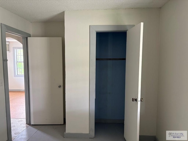 unfurnished bedroom featuring arched walkways, a textured ceiling, and a closet