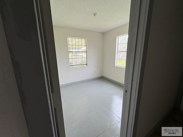 empty room featuring baseboards, finished concrete floors, and a textured ceiling