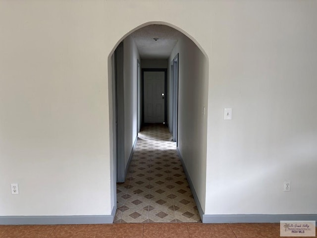 hallway with arched walkways, baseboards, and light tile patterned floors