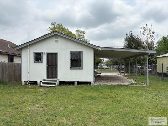 back of house with fence, entry steps, a yard, and a carport