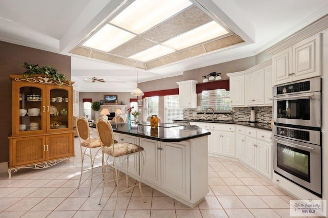 kitchen featuring a breakfast bar, white cabinets, decorative backsplash, a center island, and light tile patterned floors