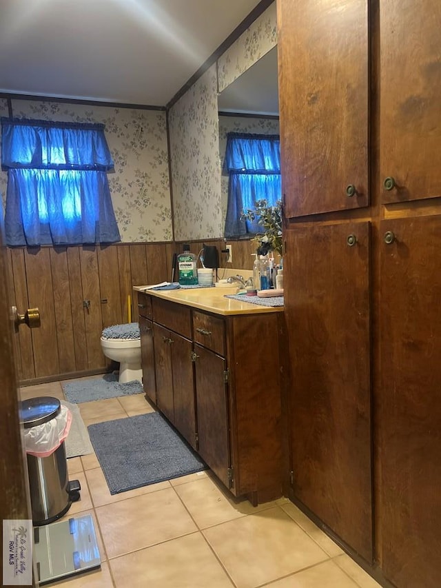 bathroom with wallpapered walls, wainscoting, toilet, tile patterned flooring, and vanity