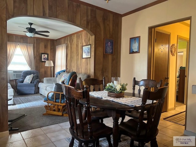 dining space with wood walls, ceiling fan, arched walkways, and light tile patterned flooring