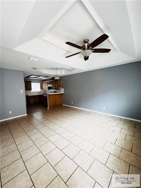 unfurnished living room featuring light tile patterned flooring, ceiling fan, baseboards, and a tray ceiling