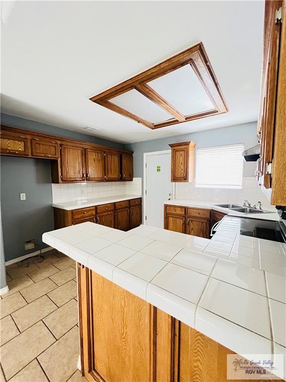 kitchen with backsplash, tile countertops, light tile patterned floors, a peninsula, and brown cabinetry