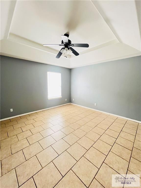 spare room featuring a raised ceiling, light tile patterned floors, baseboards, and ceiling fan